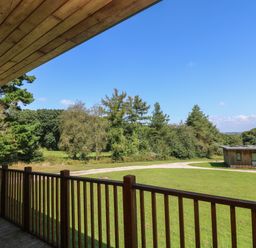 A wooden balcony overlooking a grassy area with trees and a wooden building at Hazel in Truro