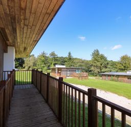 A wooden balcony overlooking grass and gravel path with two modern wooden cabins at Juniper in Truro