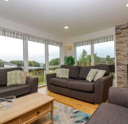 A living room with gray sofas a wooden coffee table a fireplace and large windows showing an outdoor view at Maple in Truro