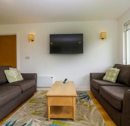A living room with two brown sofas a wooden coffee table and a wall-mounted television at Maple in Truro