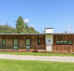 A single story wooden house with ramp and windows surrounded by grass at Maple in Truro