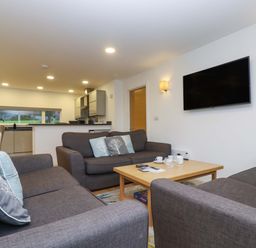 A living room with three grey sofas around a wooden coffee table and a wall-mounted TV at Oak in Truro