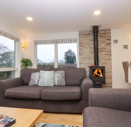 A living room with a gray sofa and cushions next to a wood burning stove and dining area at Oak in Truro