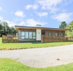 A wooden house with large windows and a fenced ramp on a grassy plot with a gravel driveway at Rowan in Truro