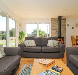 A living room with gray sofas and cushions around a wooden coffee table near a fireplace and dining area at Rowan in Truro