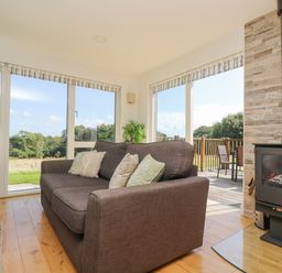 A living room with a brown sofa near large windows and a black wood-burning stove at Rowan in Truro