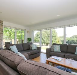 A living room with sofas pillows fireplace and large windows overlooking trees at Willow in Truro