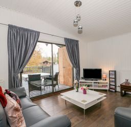 A living room with leather sofas a white coffee table a tv on a stand and glass sliding doors to a balcony at Sunset Lodge in Tattershall