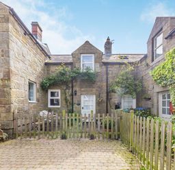A stone courtyard with wooden fences and green plants outside a stone house at Briar Cottage in Edlingham