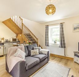 An open living room and kitchen with gray sofa dining table wooden stairs and television at Briar Cottage in Edlingham