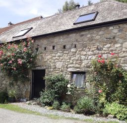 Stone barn exterior with two skylights a black door and window surrounded by rose bushes at Water Barn in Manaton near Lustleigh