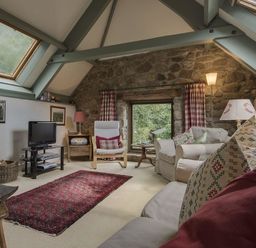 A living room with a stone wall small window sofas armchair TV and skylights at Water Barn in Manaton near Lustleigh