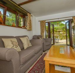 A living room with a sofa armchair wooden coffee table and television with open doors to an outdoor seating area at Buster Barn in Sampford Spiney near Tavistock