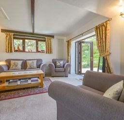 A living room with a sofa armchair wooden coffee table and floral curtains at Buster Barn in Sampford Spiney near Tavistock
