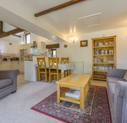 A living room with two armchairs a sofa a wooden coffee table with magazines a bookshelf and a dining table with chairs at Buster Barn in Sampford Spiney near Tavistock