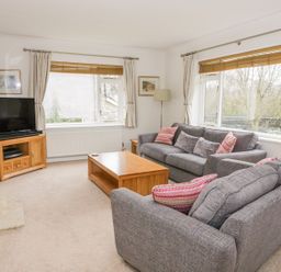 A living room with two gray sofas a wooden coffee table a TV on a stand and windows with curtains at The Dene in Betws-y-Coed