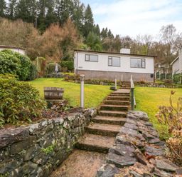 Stone steps leading up through a garden to a single-story house with a brick base at The Dene in Betws-y-Coed