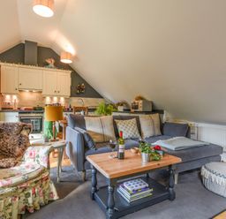 A living area with a floral armchair a gray sofa wooden coffee table and kitchen cabinets at The Linhay in Lydford