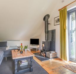 A living room with a wood stove a television a grey sofa and a wooden coffee table at The Linhay in Lydford