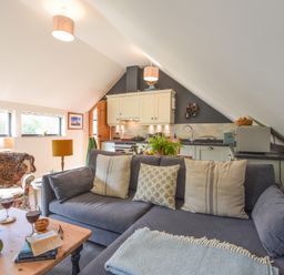 A living area with a blue sofa and pillows a wooden table with wine glasses books plants and a floral armchair at The Linhay in Lydford
