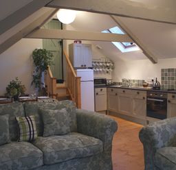 A kitchen and living area with a staircase a fridge and patterned sofas at The Stone Barn Cottage in Holne