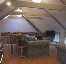 An attic living space with a floral sofa set a wood stove a television and kitchen area at The Stone Barn Cottage in Holne