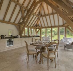 A kitchen and dining area with wooden beams a round dining table four chairs a sofa and an armchair at Cullaford Cottage in Scorriton near Ashburton
