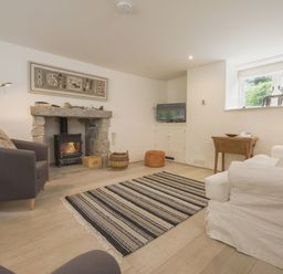A living room with a fireplace a gray armchair a white sofa a television and a striped rug at Cullaford Cottage in Scorriton near Ashburton