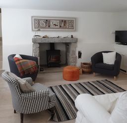 A living room with a fireplace three armchairs a striped rug and a television at Cullaford Cottage in Scorriton near Ashburton