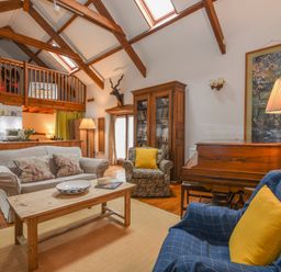 A living room with wooden beams a sofa armchairs a coffee table a piano and a wooden bookshelf at Townend Barn in Lydford