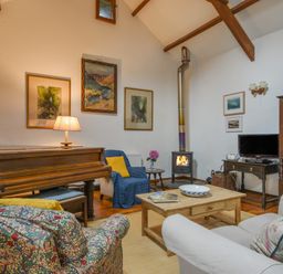 A living room with a piano armchairs a wood stove and a coffee table at Townend Barn in Lydford
