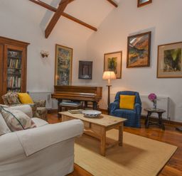 A living room with a piano a wooden coffee table and armchairs at Townend Barn in Lydford
