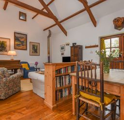 A living room with wooden beams wooden dining table flowers on table and bookshelf at Townend Barn in Lydford