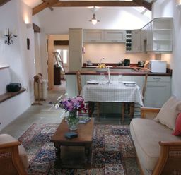 A combined kitchen and living room with a dining table set for two and a coffee table with flowers at Burham Barn in Dousland near Yelverton