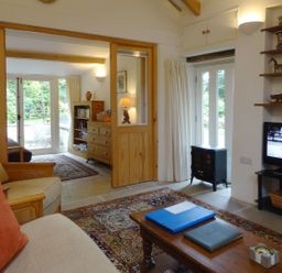 A living room with sofa chairs coffee table television and shelves at Burham Barn in Dousland near Yelverton