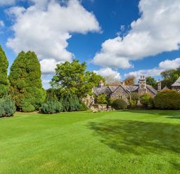 A large lawn with trees and a stone house in the background at Great Bidlake Manor in Bridestowe near Lydford