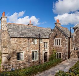 An exterior view of a stone building with multiple chimneys and windows surrounded by greenery at Great Bidlake Manor in Bridestowe near Lydford