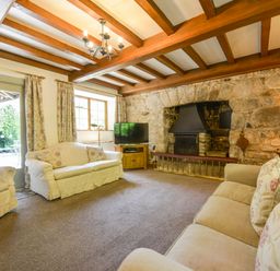 A living room with sofas a stone fireplace wooden beams and a television at Bagtor Mill in Ilsington near Haytor Vale