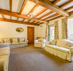 A living room with three sofas with floral cushions wooden beams on ceiling and a wooden door at Bagtor Mill in Ilsington near Haytor Vale