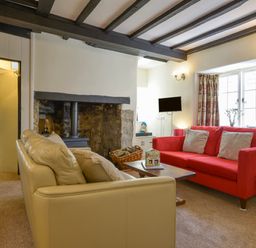 A living room with a beige sofa a red sofa a wooden coffee table and a fireplace at Little Gate Cottage in North Bovey