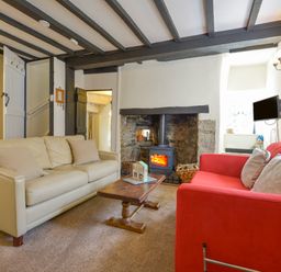 A living room with a beige sofa a red sofa a wood burning stove and a wooden coffee table at Little Gate Cottage in North Bovey