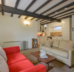 A living room with red and beige sofas and a wooden coffee table near a kitchen with white cabinets at Little Gate Cottage in North Bovey