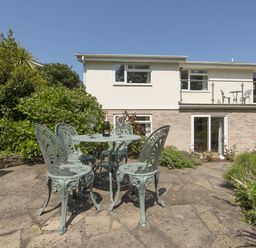 A patio with a metal table and four chairs with a bottle and glasses in a garden at Exe View in Dawlish