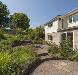 A garden with stone steps and patio next to a two story house with balcony at Exe View in Dawlish