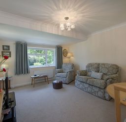 A living room with a patterned sofa and armchair a window with curtains a small table a lamp and a dining table at Exe View in Dawlish
