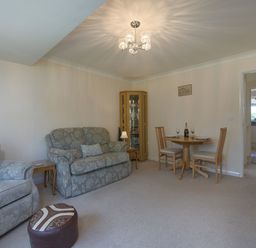 A living room with two sofas a small round dining table with two chairs and a glass cabinet at Exe View in Dawlish