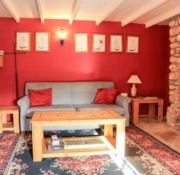 A living room with a blue sofa and red cushions wooden tables a stone fireplace and framed pictures on a red wall at Sandridge Barton in Stoke Gabriel