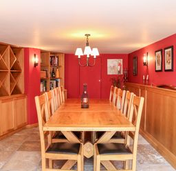 A dining room with a wooden table and chairs with red walls and built in wooden shelves at Sandridge Barton in Stoke Gabriel