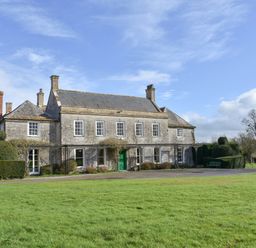 An exterior view of a stone house with multiple chimneys a green door and trimmed hedges in front at Wootton House in Butleigh Wootton near Compton Dundon
