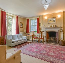 A living room with a fireplace red curtains armchairs a gray sofa and a large patterned rug at Wootton House in Butleigh Wootton near Compton Dundon